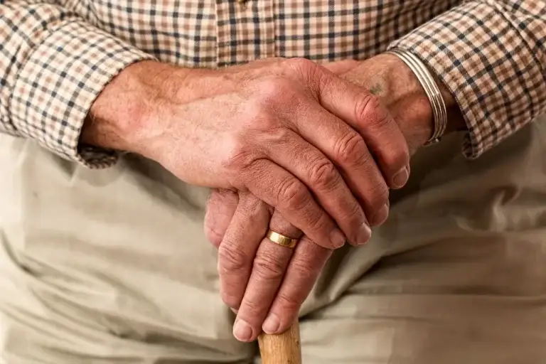 Mãos de um homem idoso segurando uma bengala.