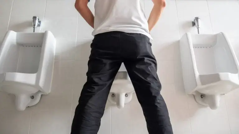 Homem de costas em um mictório.